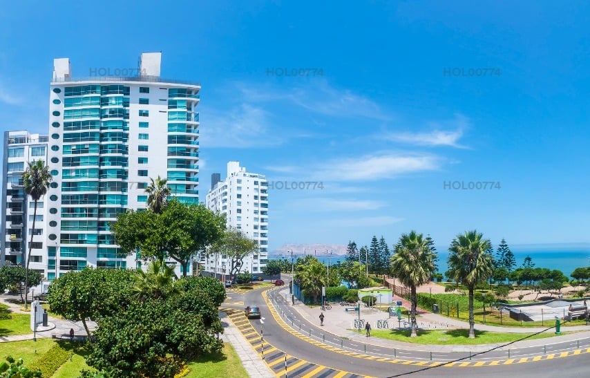 Modern beachfront high-rise residential buildings with palm trees, curved street, and ocean view under clear blue sky