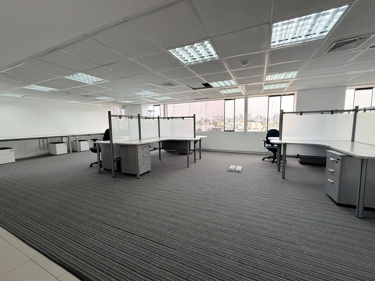 Modern open office space with modular workstations, striped gray flooring, and large windows with city views