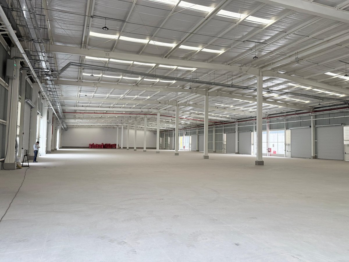 Empty industrial warehouse interior with concrete floor, metal support columns, and fluorescent ceiling lights