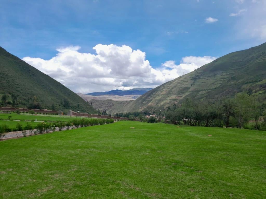 Lush green valley surrounded by forested mountains under blue sky with white clouds and distant settlements