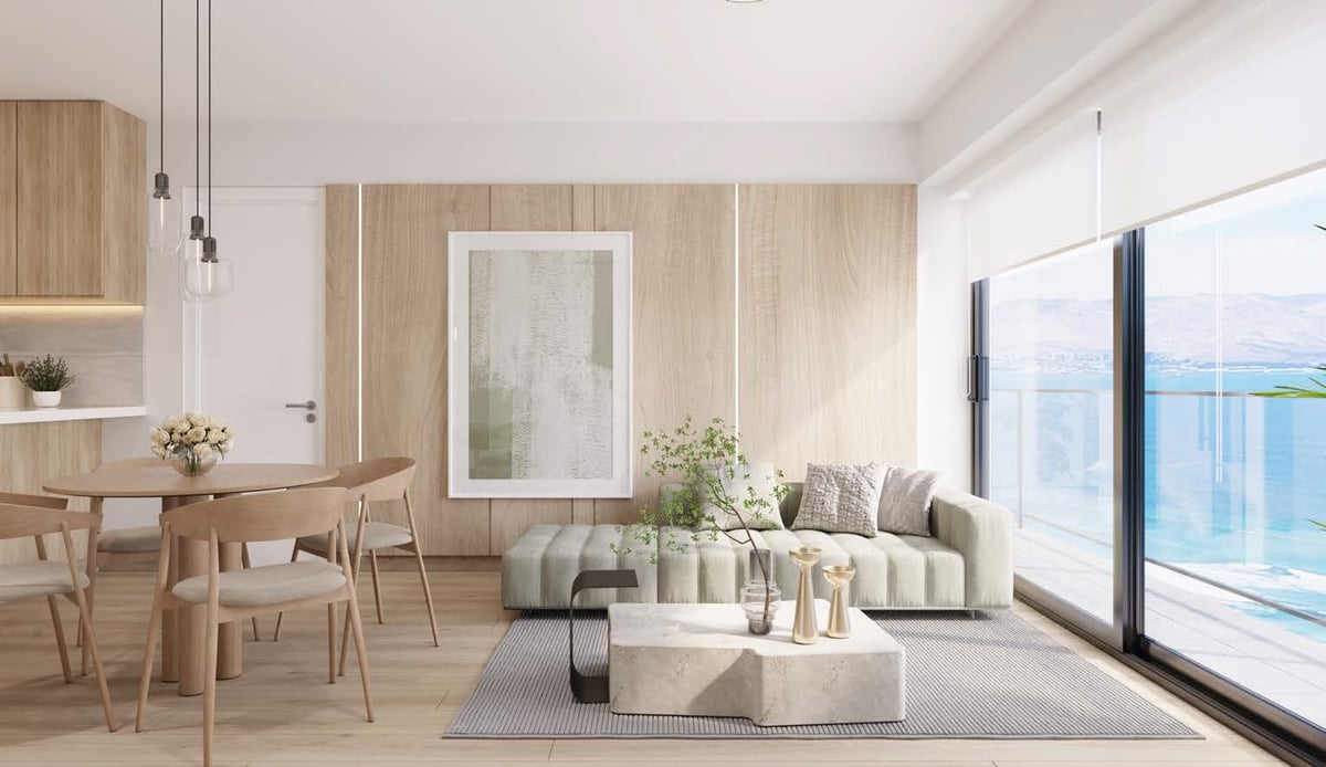 Modern beige apartment interior with dining area, living room sofa, and ocean view through large windows