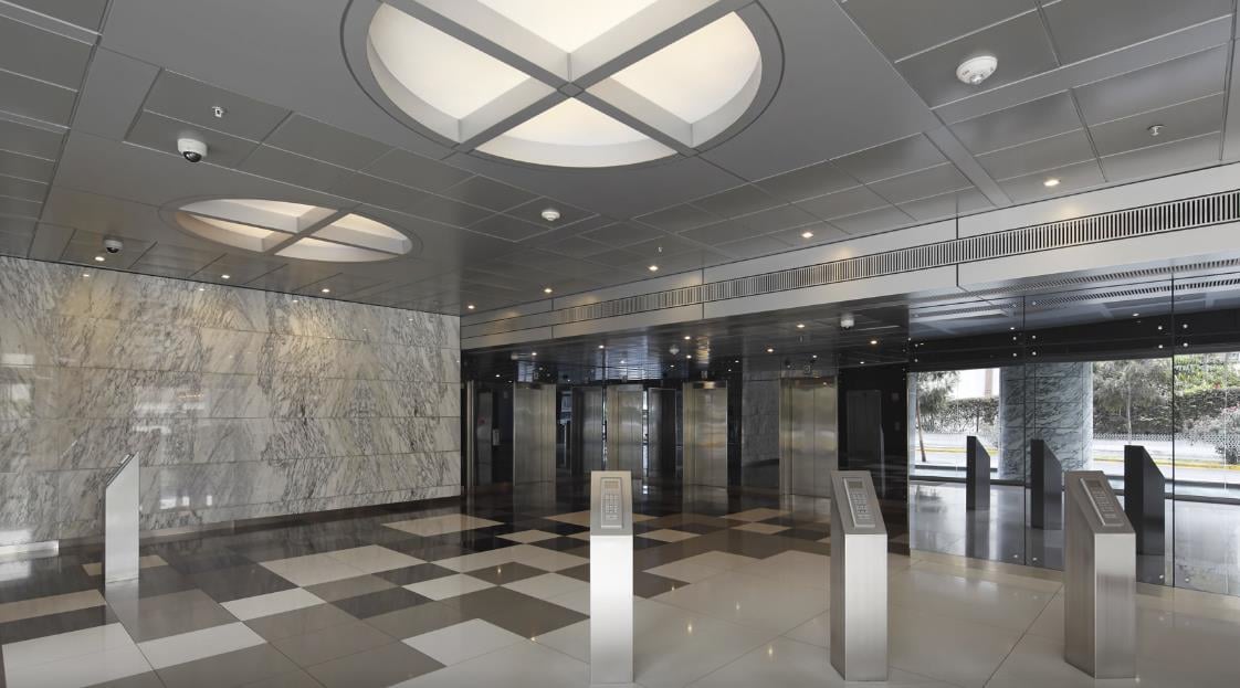 Modern building lobby with geometric ceiling lights, marble walls, polished floor, and glass elevator doors