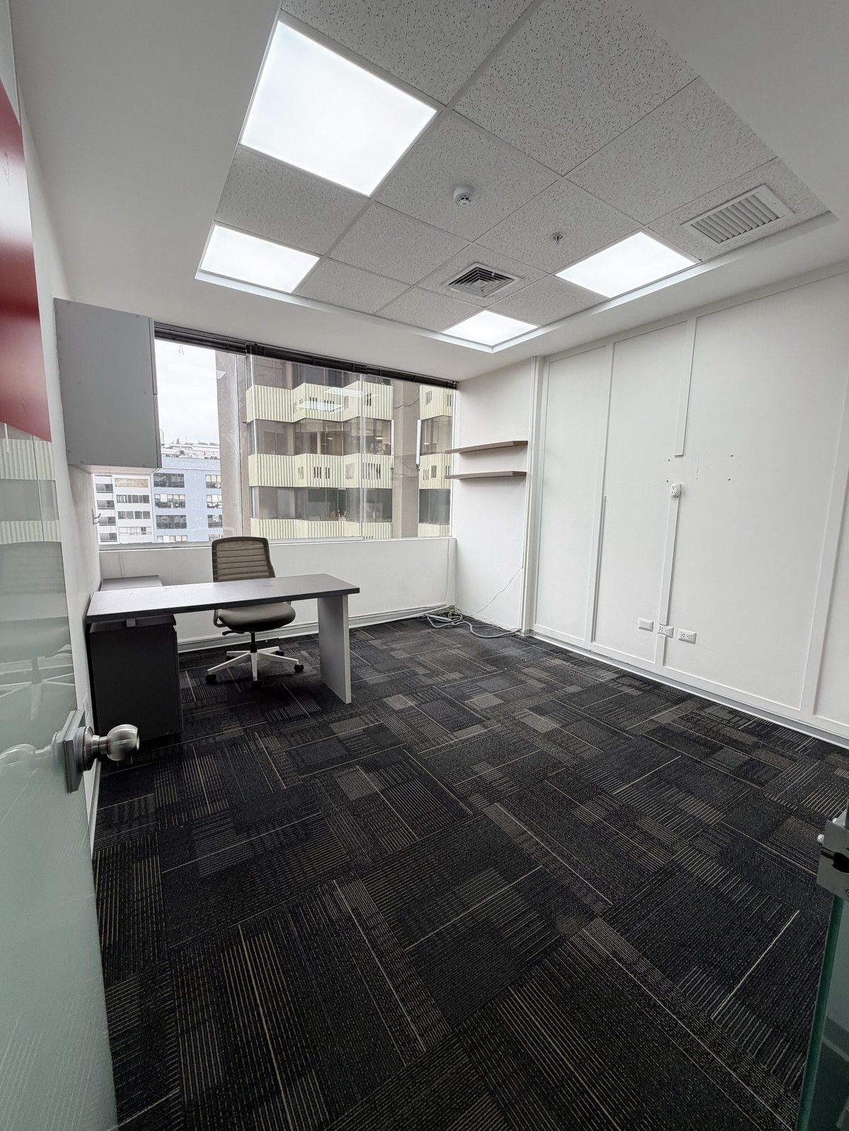 Modern office space with white desk, glass partitions, black tile flooring, and bright ceiling lights overlooking city buildings
