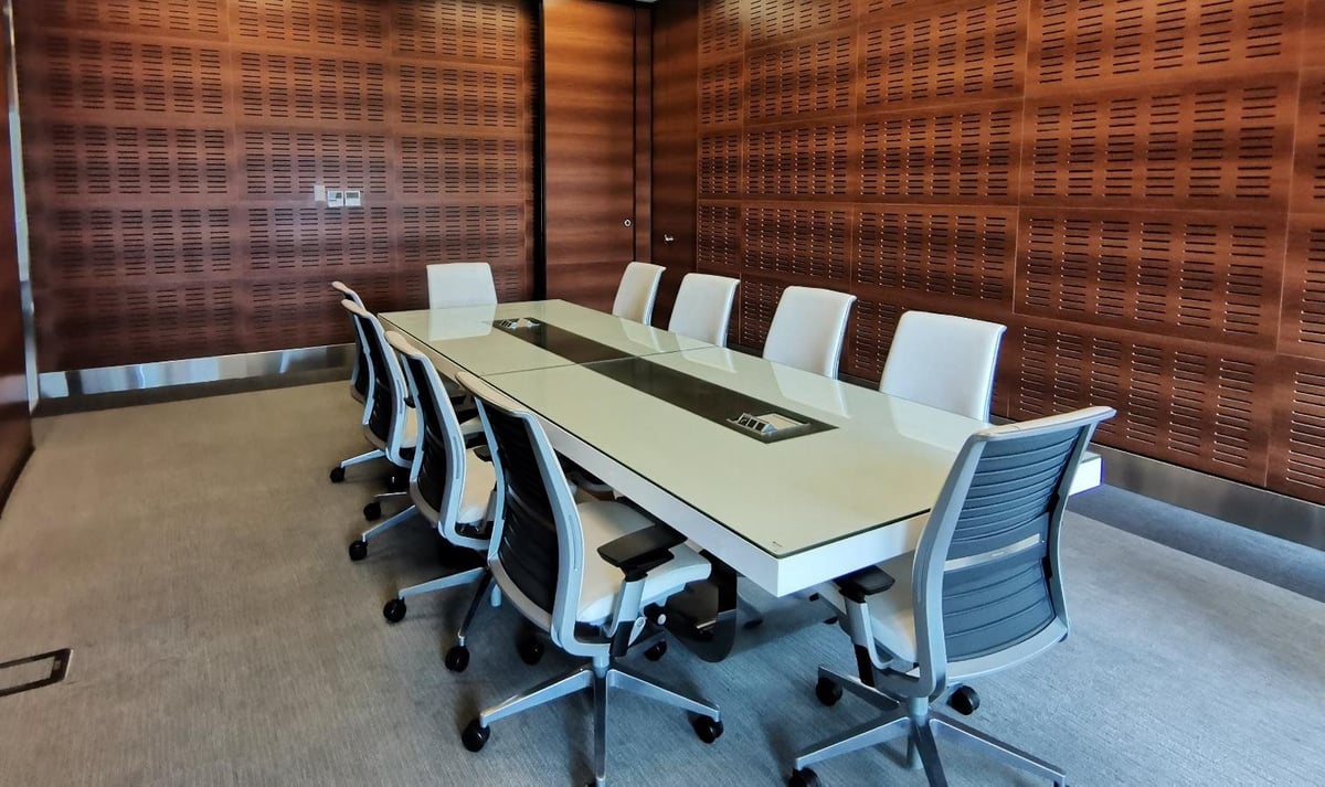 Modern conference room with long white table, white and blue office chairs, and acoustic wood-paneled walls