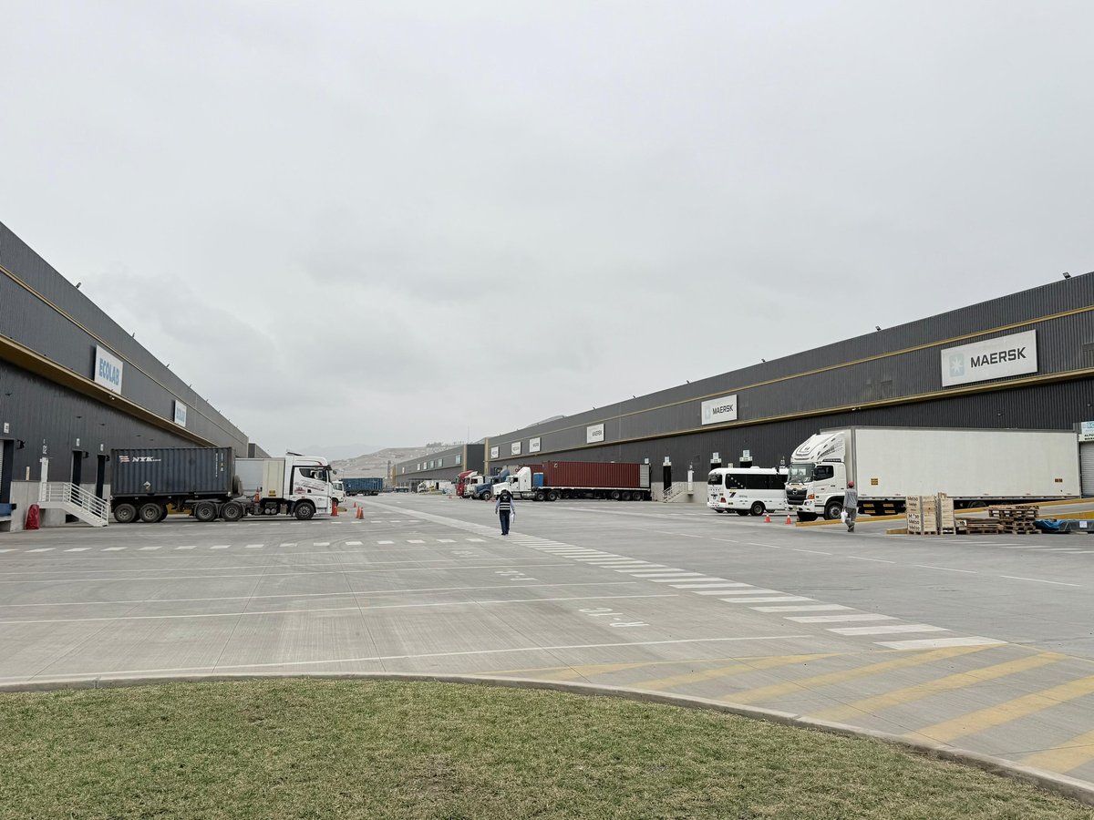 Industrial warehouse facility with large trucks parked on asphalt lot, dark cloudy sky overhead