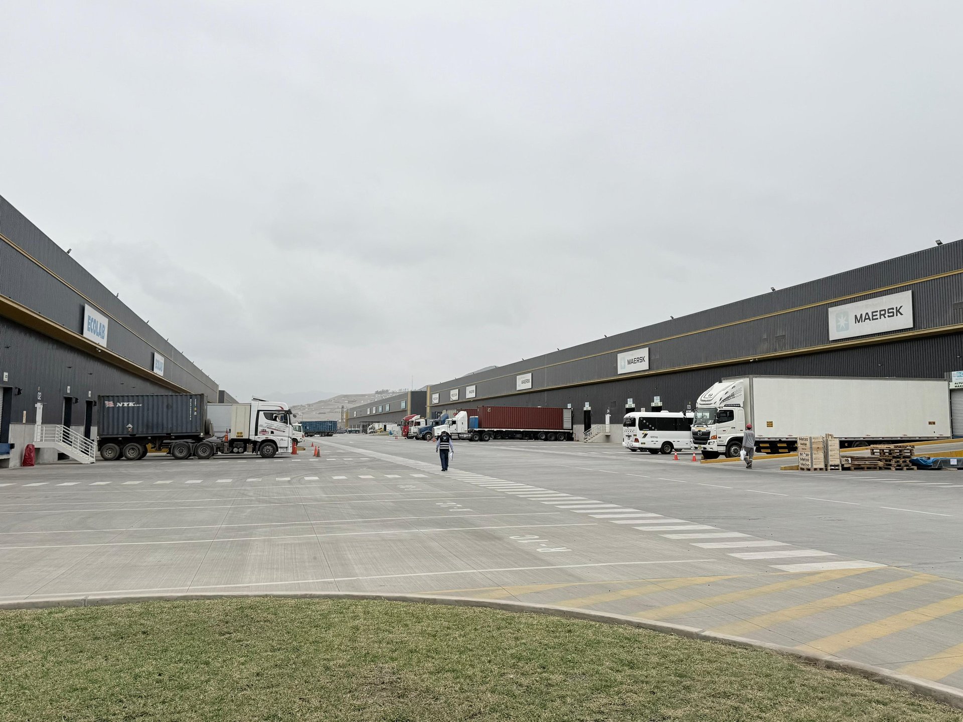Industrial warehouse facility with large trucks parked on asphalt lot, dark cloudy sky overhead
