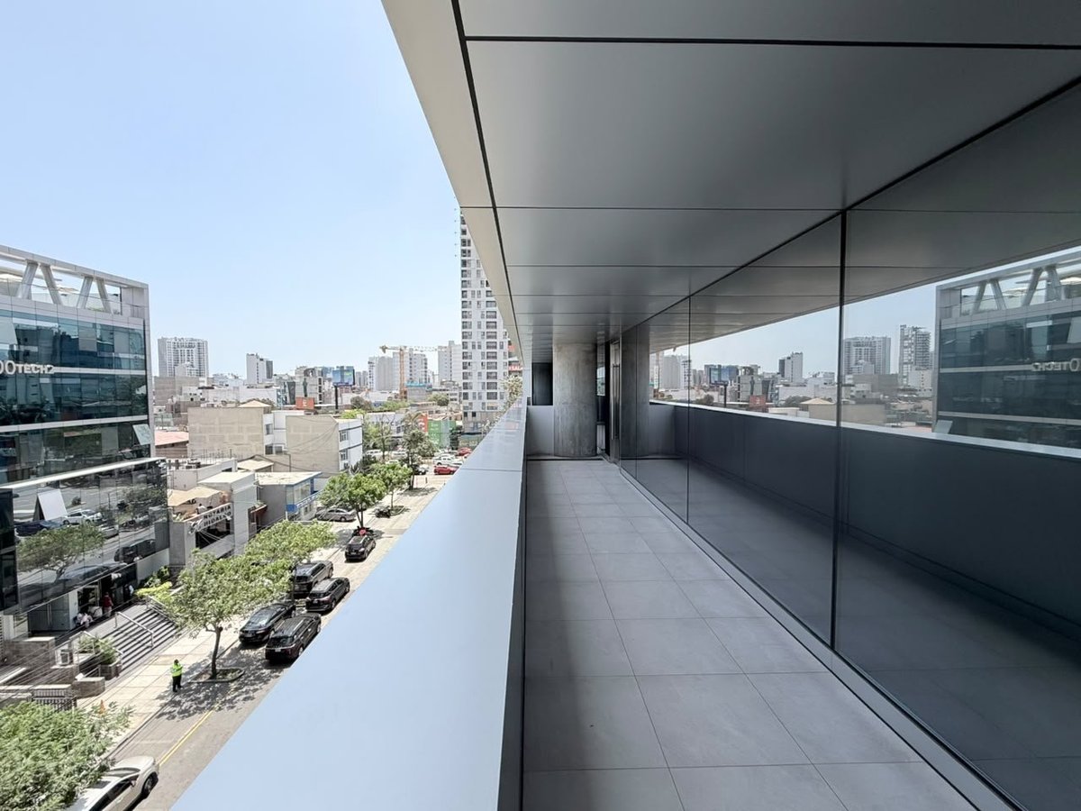 Modern high-rise balcony with glass railings overlooking an urban cityscape with buildings and streets below