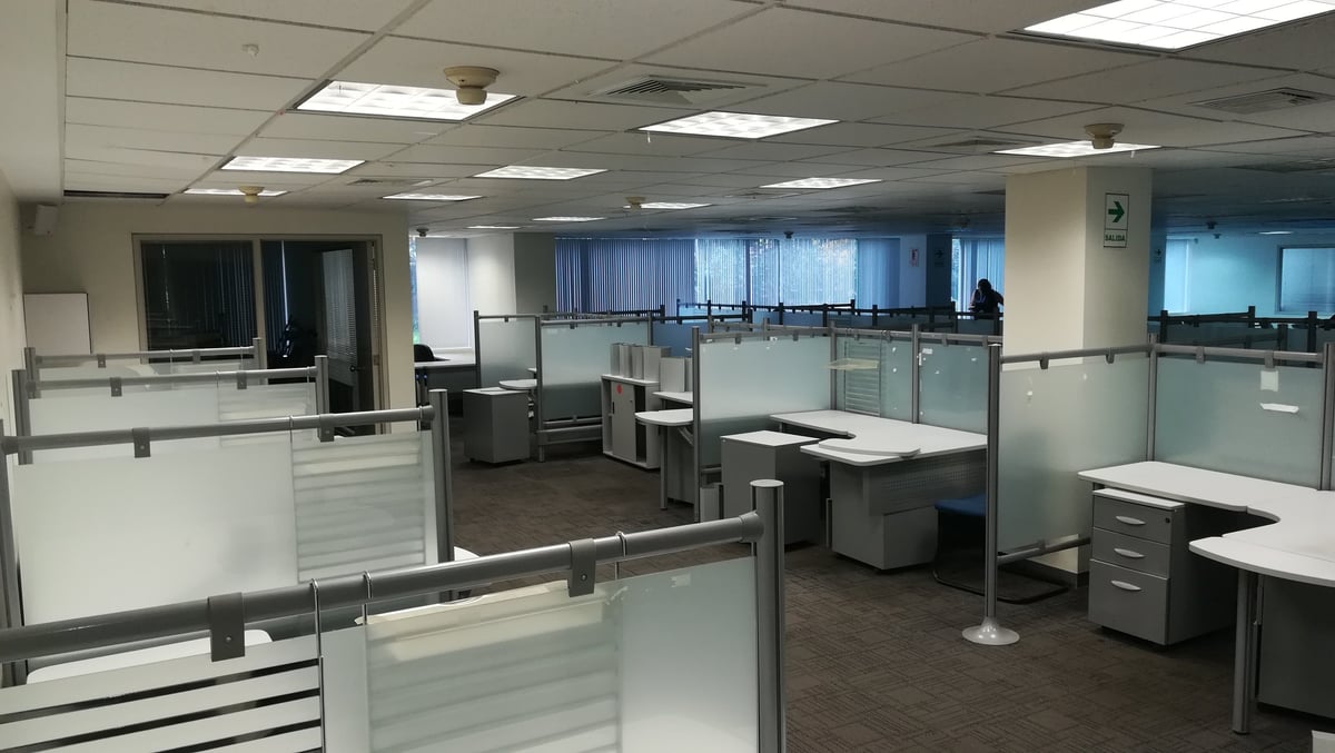 Modern office space with glass partition walls, cubicles, and workstations under fluorescent ceiling lights