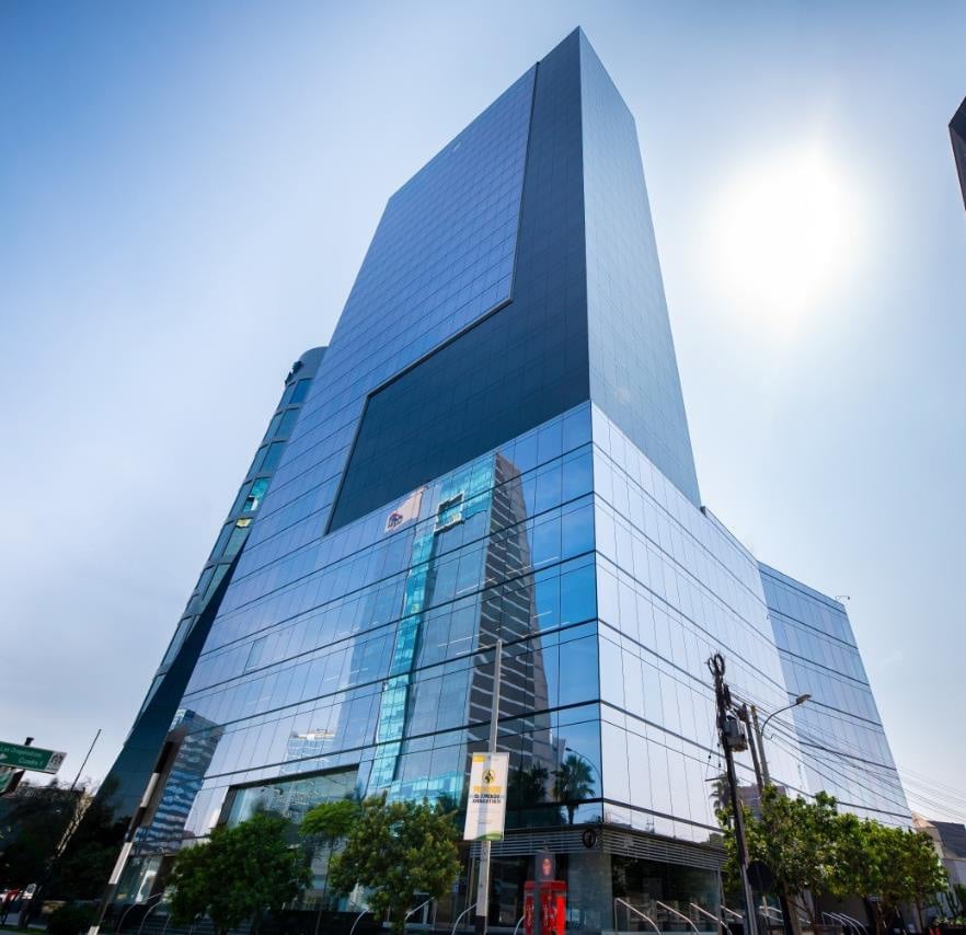 Modern glass and steel skyscraper with blue-tinted facade against bright sky, street-level entrance visible below