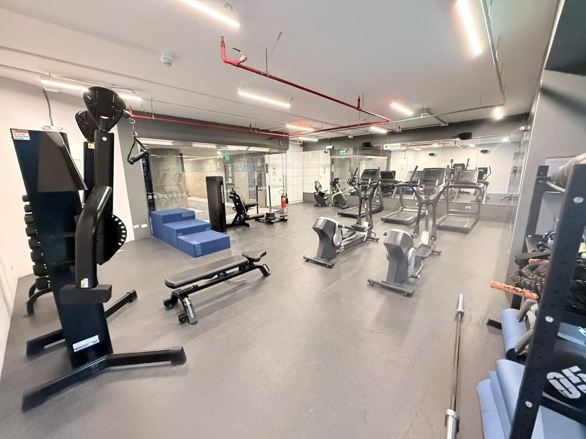 Modern gym interior with various exercise equipment including treadmills, stationary bikes, and weight machines on white flooring