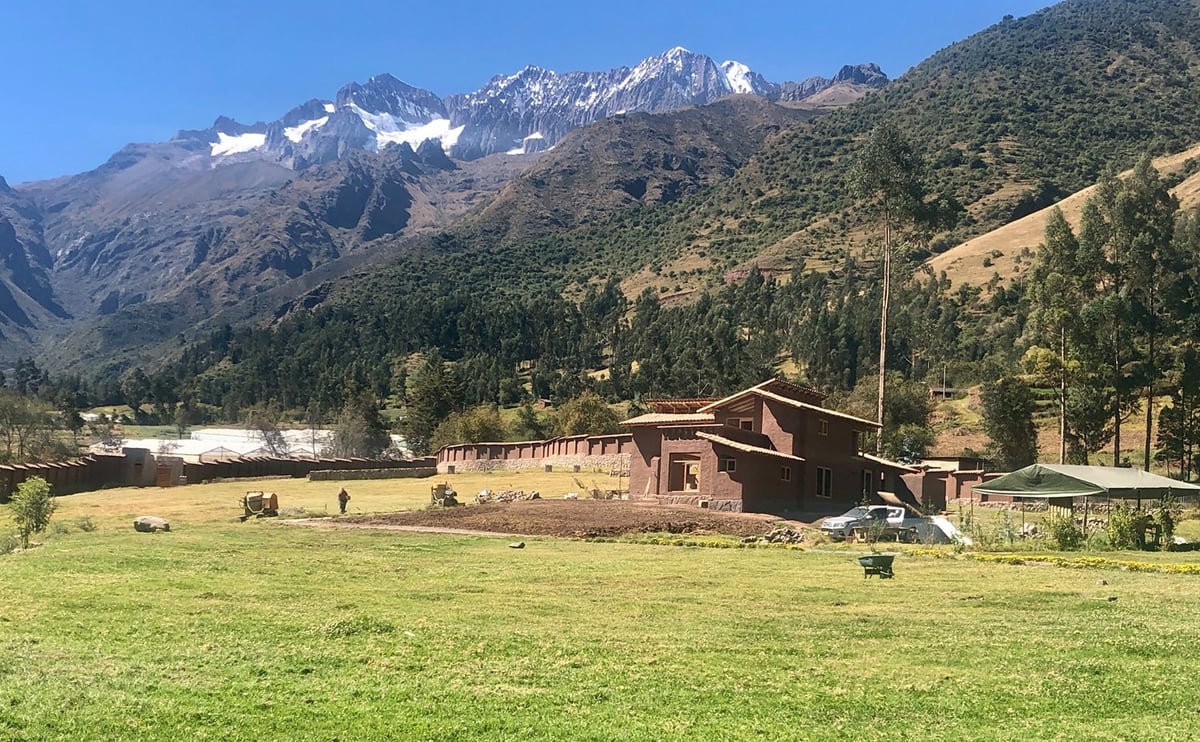Rustic barn in a green valley surrounded by snow-capped mountains and pine forest.
