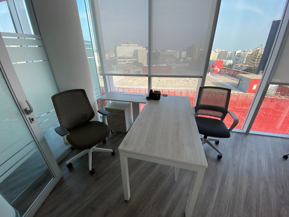 Modern office meeting room with gray desk, two black chairs, and floor-to-ceiling windows overlooking a city skyline