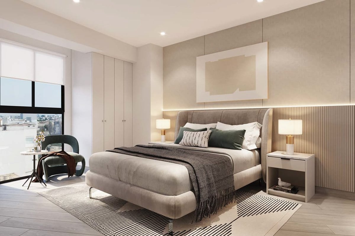 Modern bedroom with beige upholstered bed, white wardrobes, nightstands with lamps, armchair by window, and neutral color palette