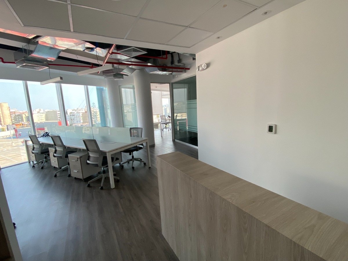 Modern office space under renovation with exposed ceiling infrastructure, office chairs, and city skyline view through floor-to-ceiling windows