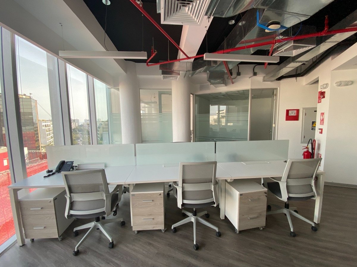 Modern office workspace with ergonomic chairs, desks, and filing cabinets overlooking a city skyline through floor-to-ceiling windows
