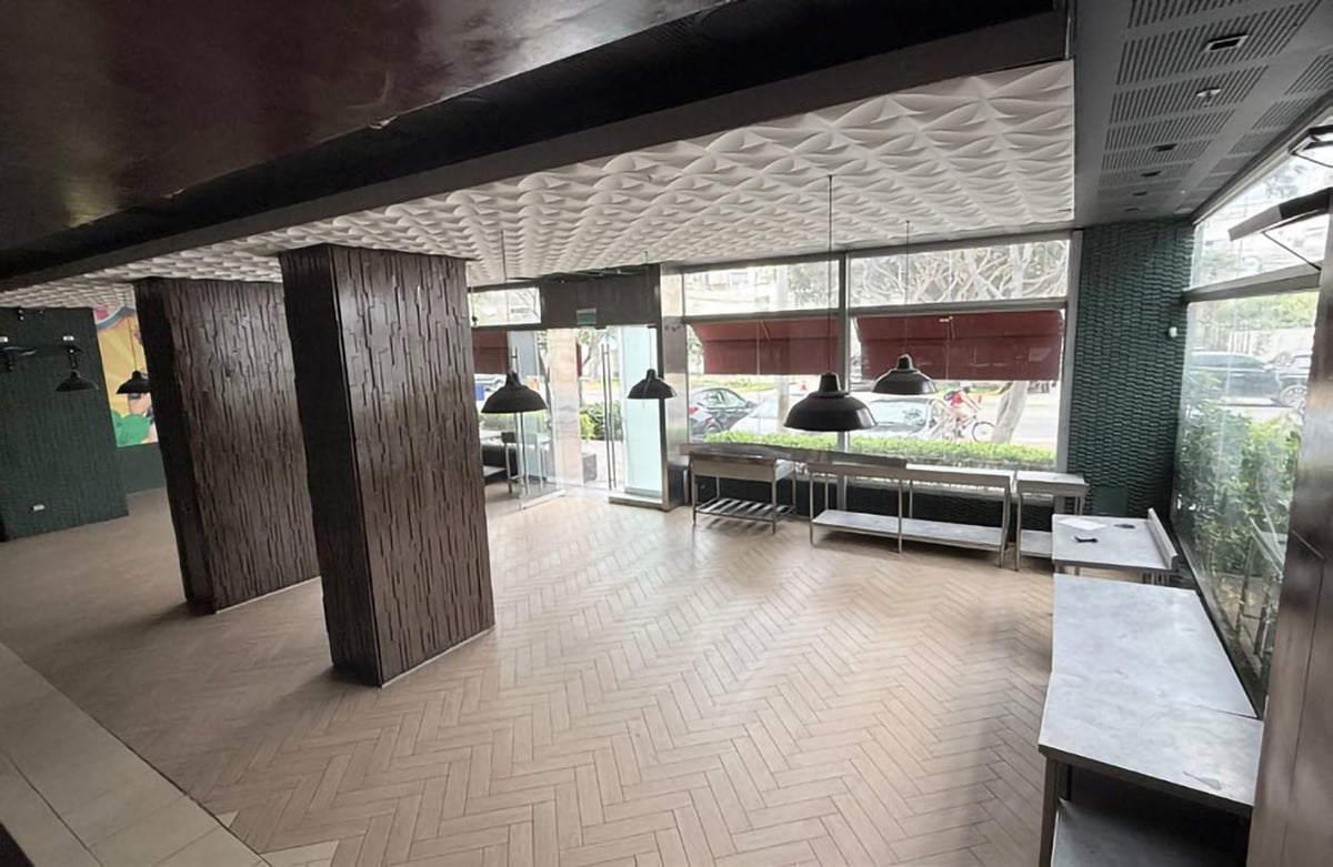 Modern open office space with herringbone flooring, wooden columns, and minimalist furnishings near large windows