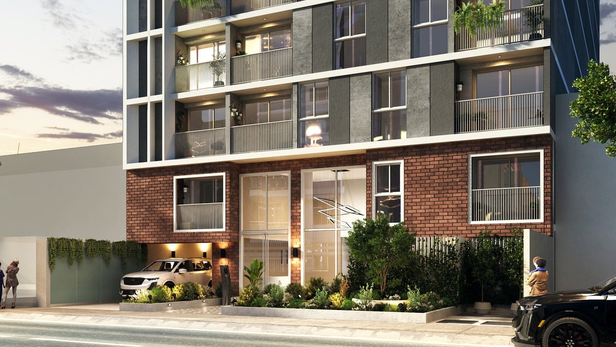 Modern mixed-use building with brick ground floor retail space and residential units above, featuring large storefront windows and green landscaping.