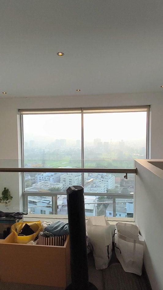High-rise apartment interior with large windows overlooking a hazy cityscape, cardboard boxes and items in foreground