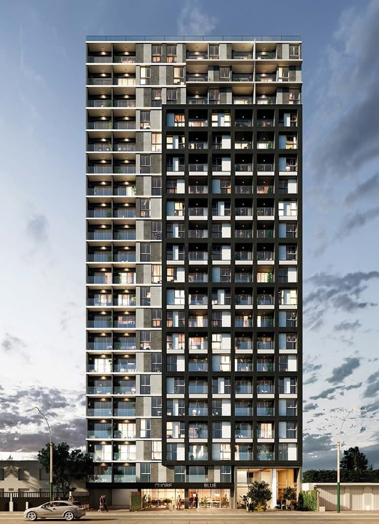 Modern residential high-rise apartment building with stacked balconies and mixed lighting, photographed at dusk against a cloudy sky