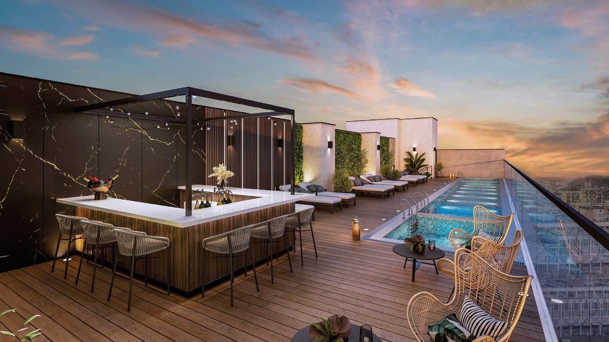 Modern rooftop terrace at sunset with outdoor bar, lounge seating, and illuminated swimming pool overlooking city skyline