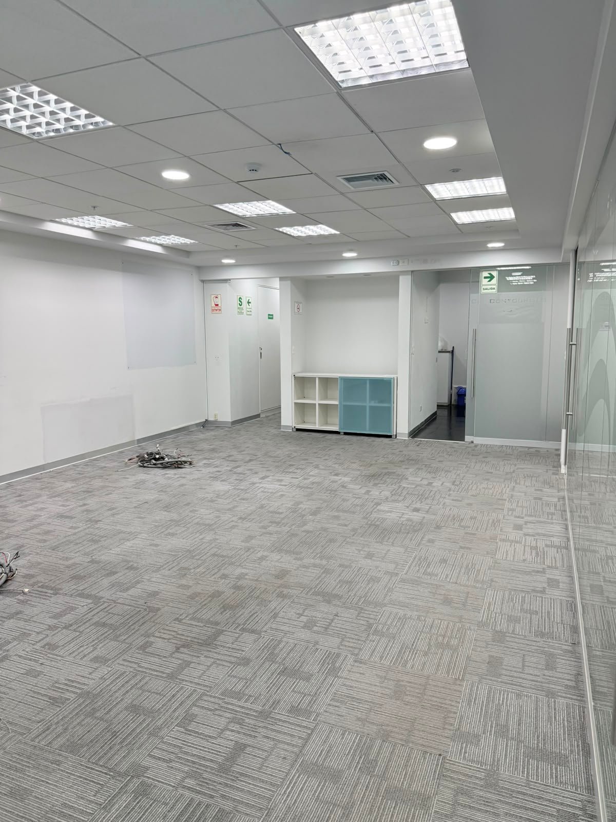 Empty modern office space with gray patterned flooring, white walls, glass partitions, and recessed ceiling lights