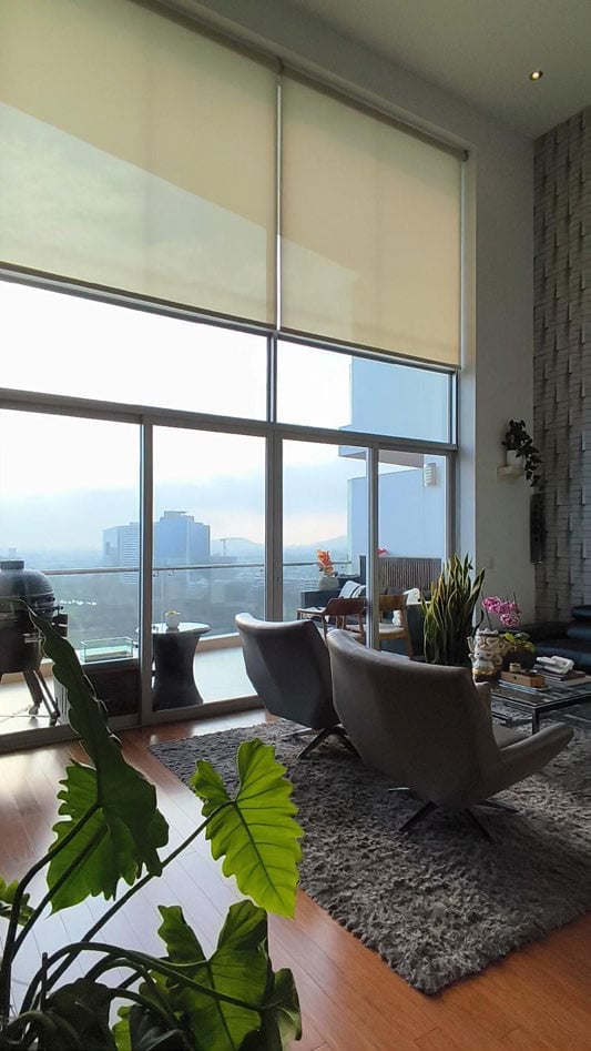 Modern high-rise apartment with floor-to-ceiling windows, gray armchair, potted plants, and city skyline view